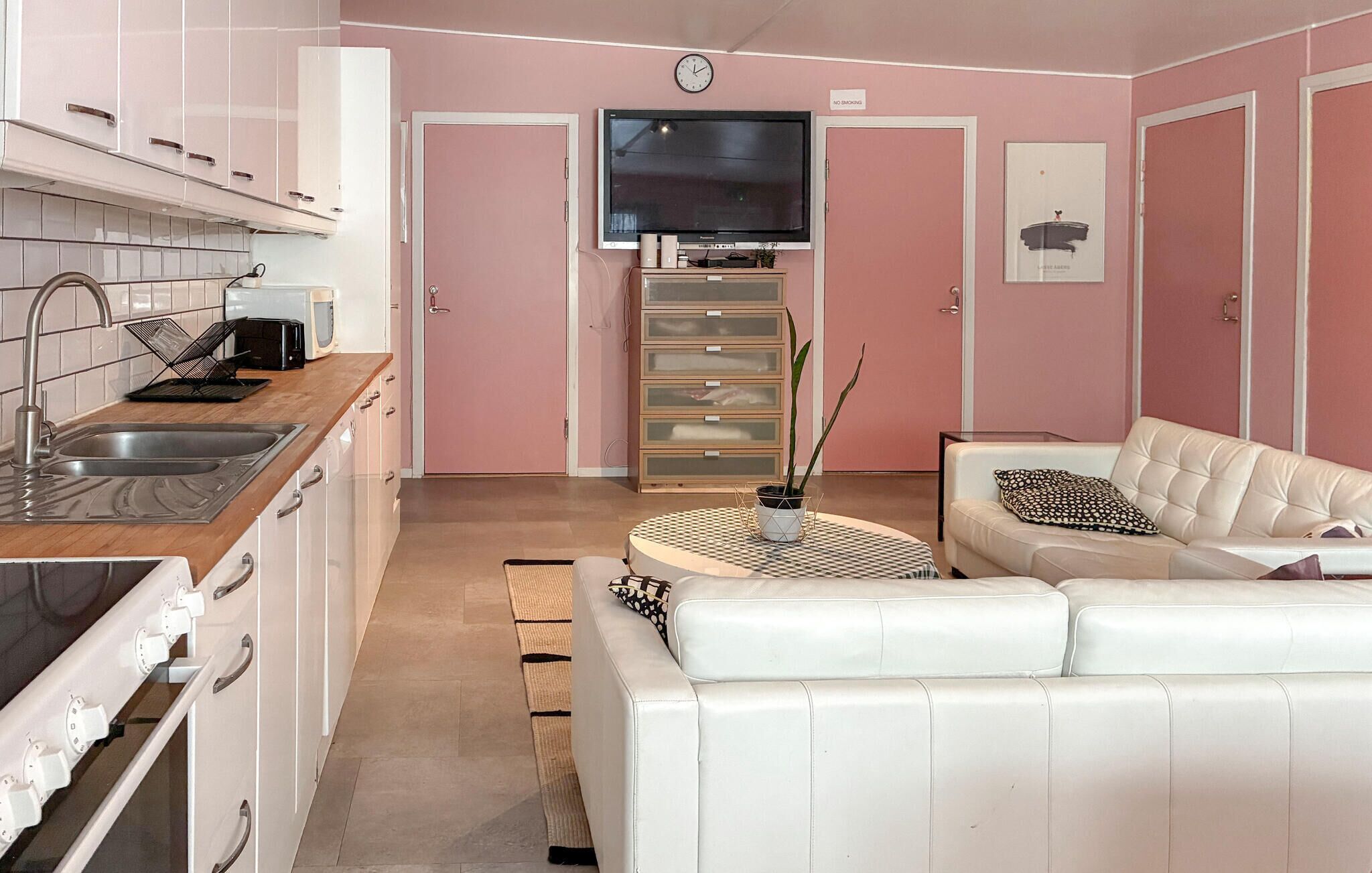 A modern kitchen with white cabinets, a stainless steel sink, and a flat-screen TV mounted above a wooden cabinet.