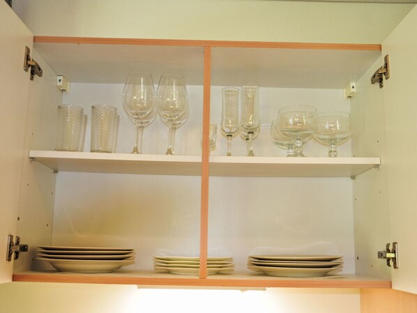 Un armario de cocina con repisas que contienen platos, tazones y copas de vino.