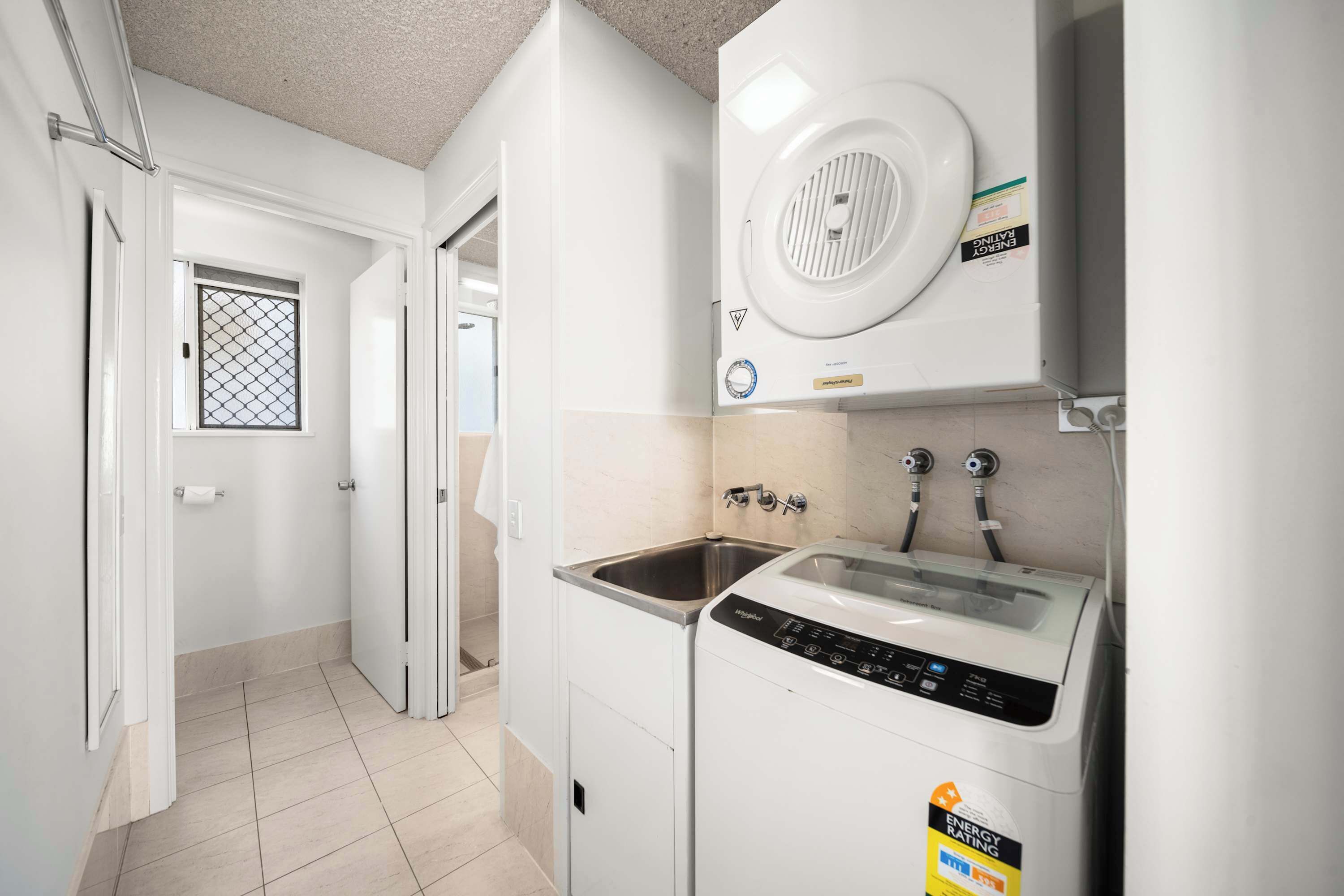 A compact kitchen with a built-in washer and dryer, a window with a metal grill, and a tiled floor.