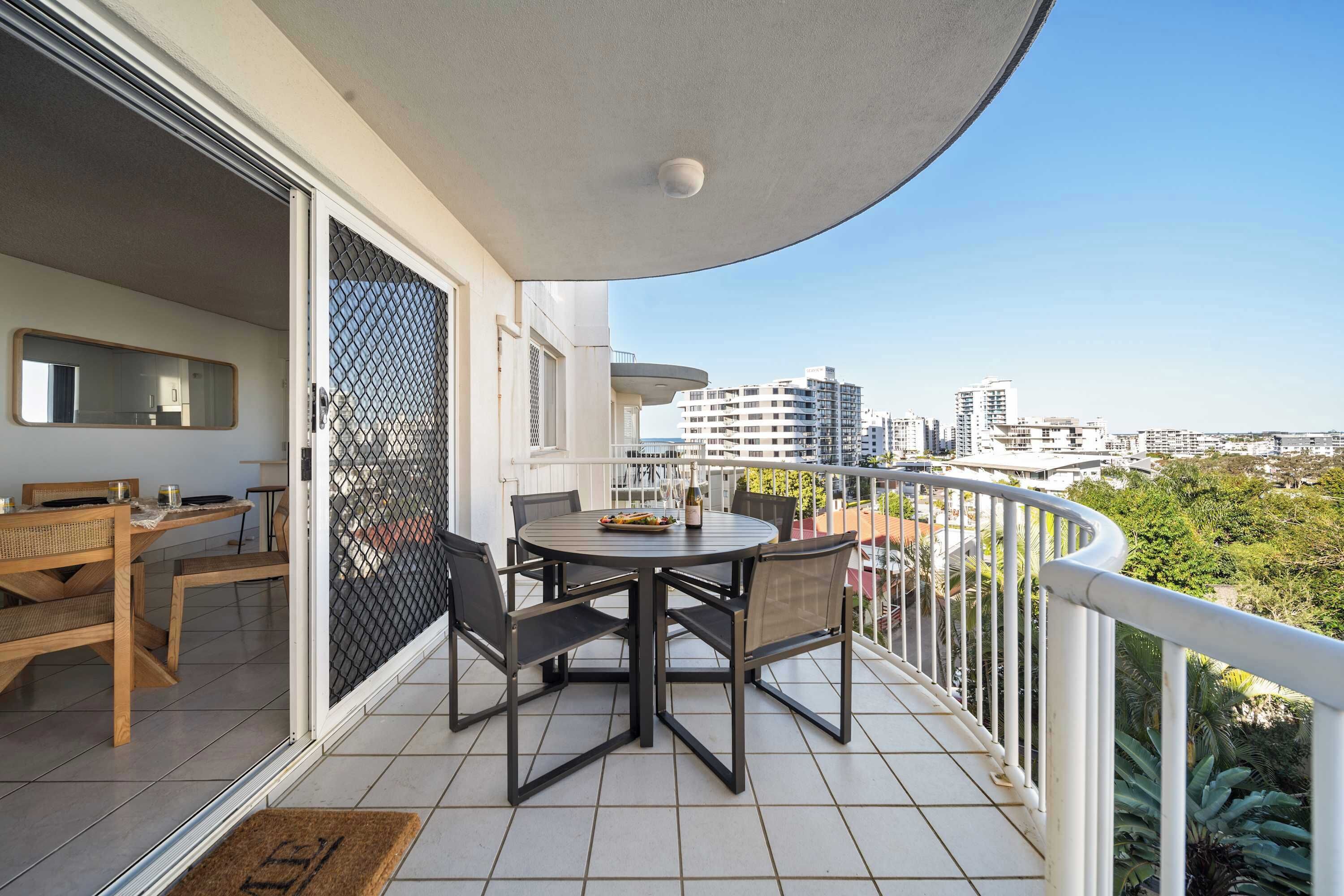 Un balcon avec une table et des chaises, une vue sur la ville, et une porte donnant sur un espace intérieur également équipé d’une table et de chaises.