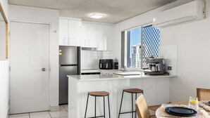A modern kitchen with white cabinets, a stainless steel refrigerator, a coffee machine, and a window with a view of buildings. - Coastal Rooftop Escape Mooloolaba - Walk to Beach (Mooloolaba Region)