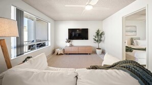 A modern bedroom with a large window, a ceiling fan, a flat-screen TV, a wooden cabinet, and a potted plant. - Coastal Rooftop Escape Mooloolaba - Walk to Beach (Mooloolaba Region)