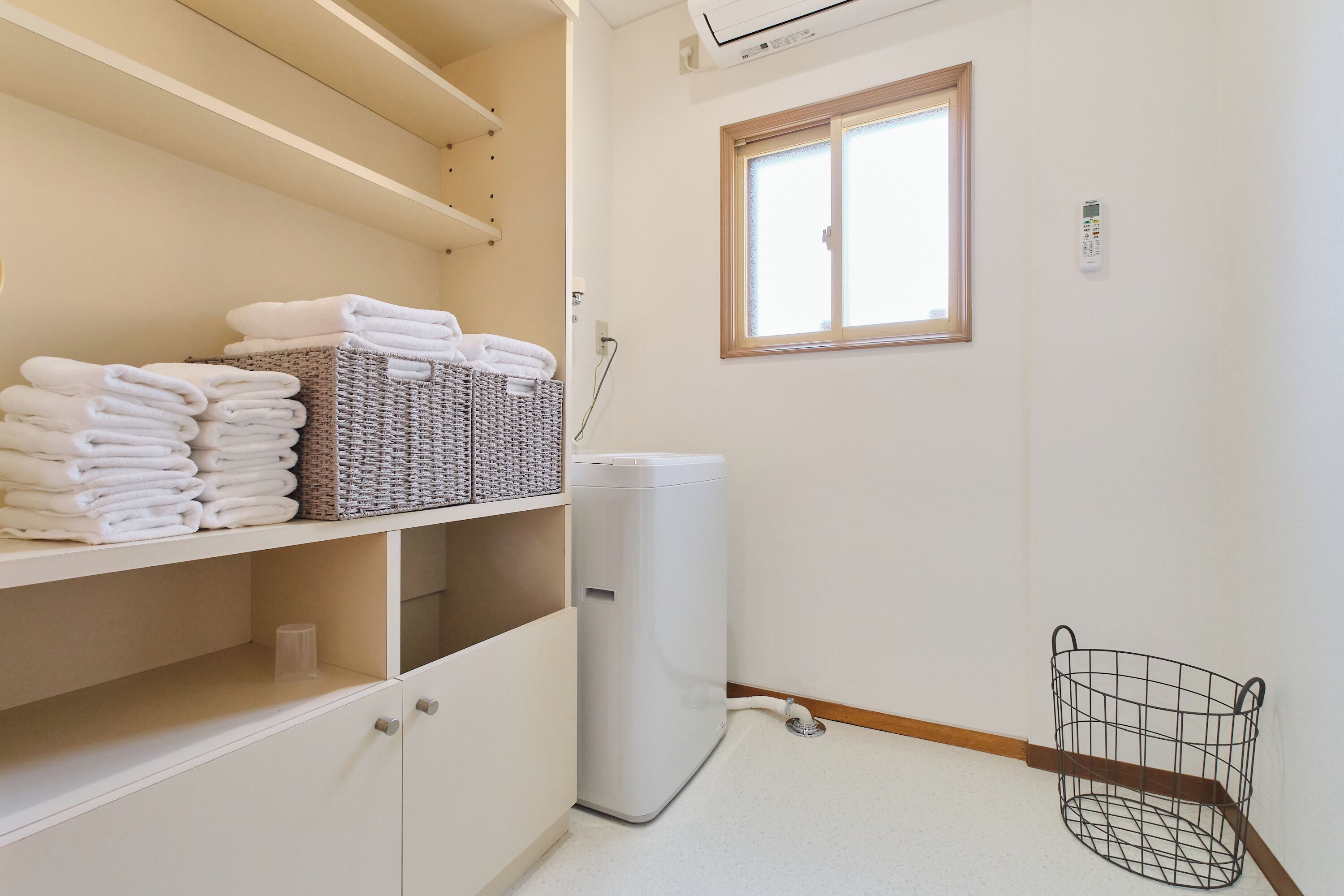 Un baño con un inodoro blanco, una cesta de toallas dobladas, una cesta de mimbre y una ventana.