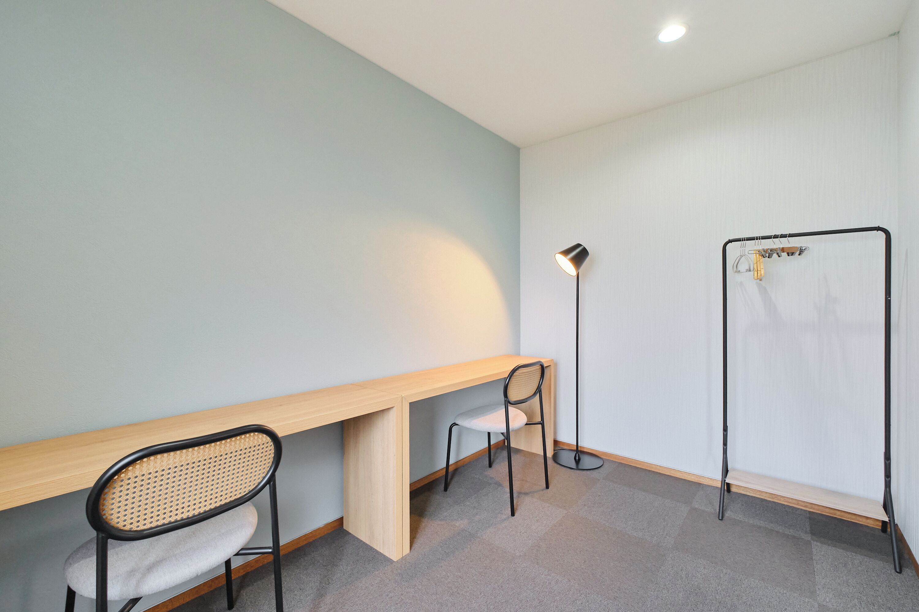 A room with a wooden desk, a chair, a floor lamp, and a clothes drying rack.