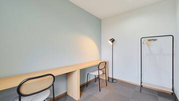 A room with a wooden desk, a chair, a floor lamp, and a clothes drying rack.