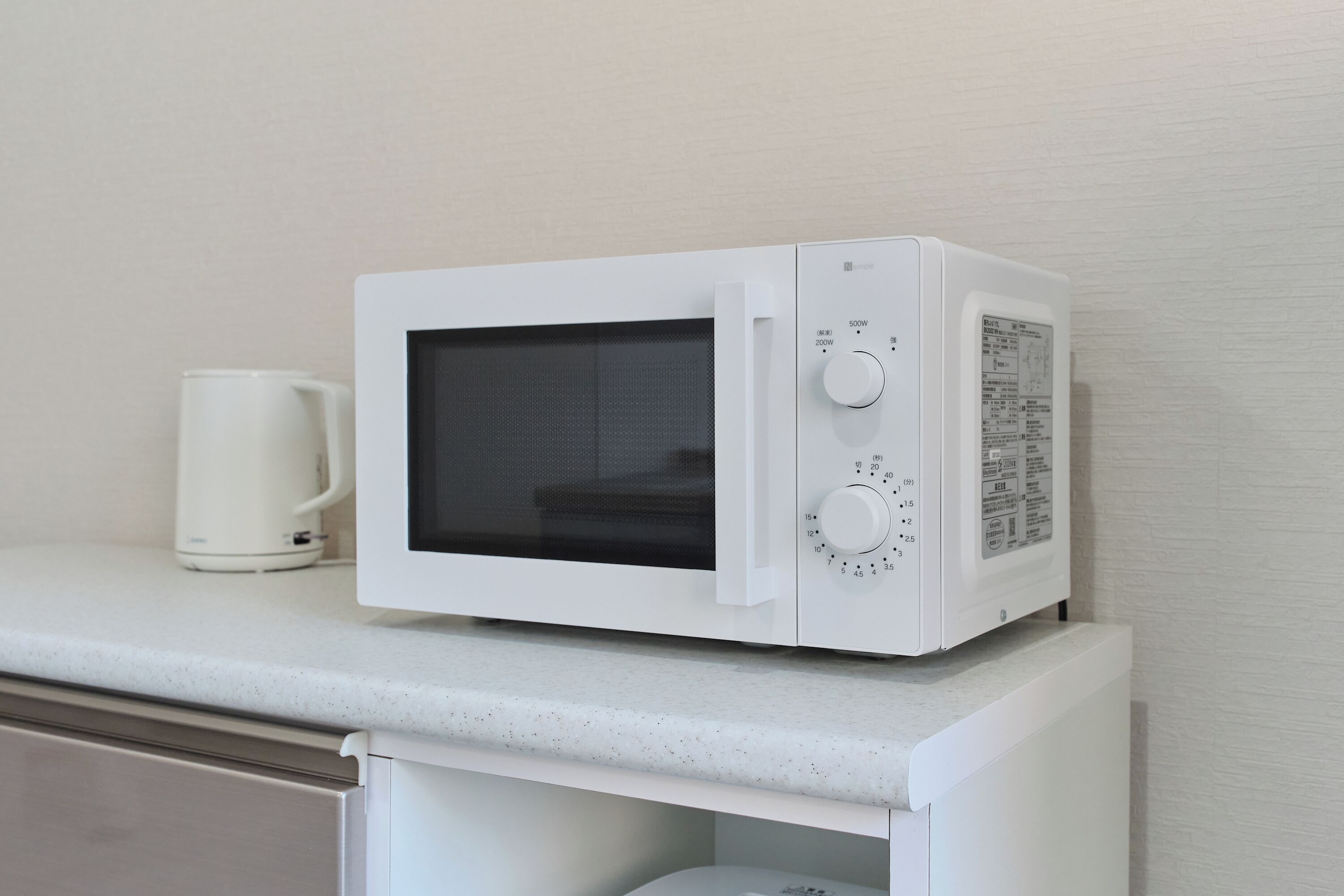 A white microwave on a countertop with a white mug beside it.