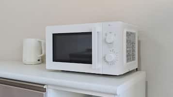 A white microwave on a countertop with a white mug beside it.