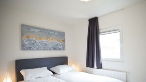 A bedroom with a bed, a nightstand, a window with curtains, and a painting on the wall. - Holiday Home in Nijkerk With Terrace (Nijkerk)