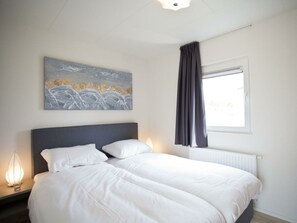Ein Schlafzimmer mit Bett, Nachttisch, einem Fenster mit Vorhängen und einem Gemälde an der Wand.