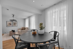 Un salon moderne avec une table à manger ronde, des chaises noires, un canapé beige et un vase blanc orné d’une plante.