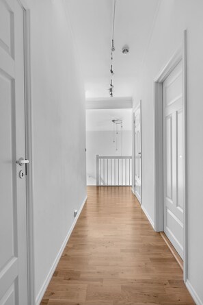 Un couloir aux murs blancs et au plancher en bois, qui mène à une porte dotée d’un trou de serrure.