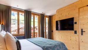 A bedroom with a bed, curtains, a TV, and a wooden wall.