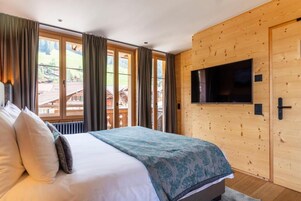 Quarto com cama, cortinas, televisão e parede de madeira.