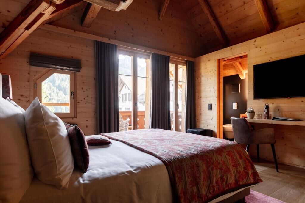 A wooden cabin bedroom with a bed, a desk, and a TV.