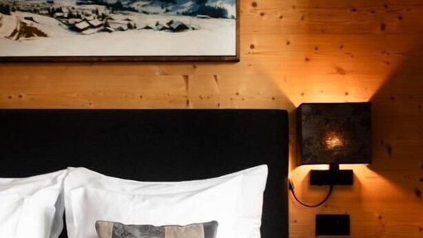 A bed with white and gray bedding, a wooden headboard, and a wall-mounted nightstand with a lamp.