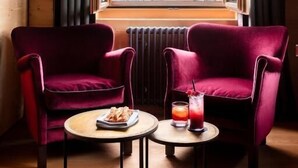 A room with two red velvet chairs, a small table with a drink and snacks, and a window with a view of a village.