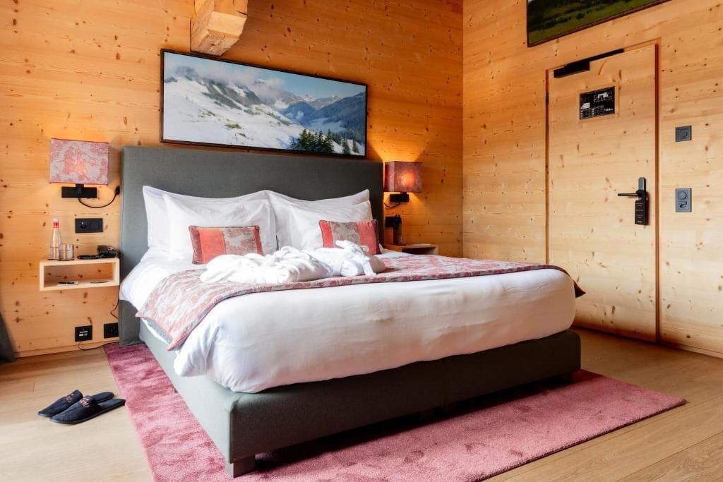 A bedroom with a bed, a nightstand, a wall-mounted TV, and a door.