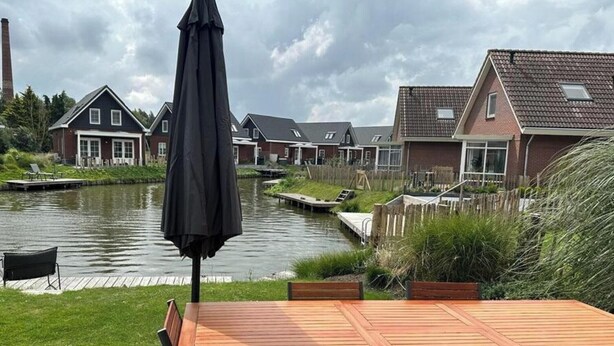 Une vue sur la rivière, avec une terrasse en bois, des sièges d’extérieur et des maisons en arrière-plan.