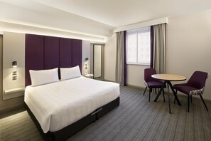 A hotel room with a large bed, a round table, two chairs, a mirror, and a window with curtains. - Premier Inn Manchester City Centre - Northern Quarter (Manchester)