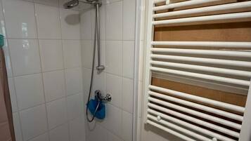 Een douche met een handdouche, een wandhanddoekhouder en een witte radiator.