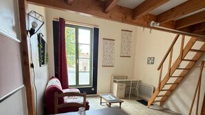 Ein gemütliches Zimmer mit Esstisch, Stühlen, einer Couch, einem Fenster mit Vorhängen, einer Treppe und einer Heizung.