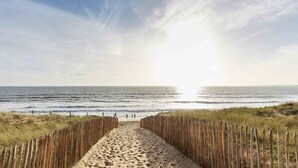 Ein Strandweg, der zum Meer führt, gesäumt von einem Holzzaun auf beiden Seiten.