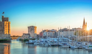 Um cais com vários barcos atracados, uma torre histórica e o topo imponente de uma igreja.