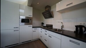 Une cuisine moderne avec des meubles blancs, un four à micro-ondes en acier inoxydable, une cuisinière à gaz et une machine à café.
