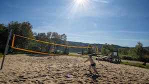 Une plage de sable avec un filet de volley-ball, une table de pique-nique et un banc.