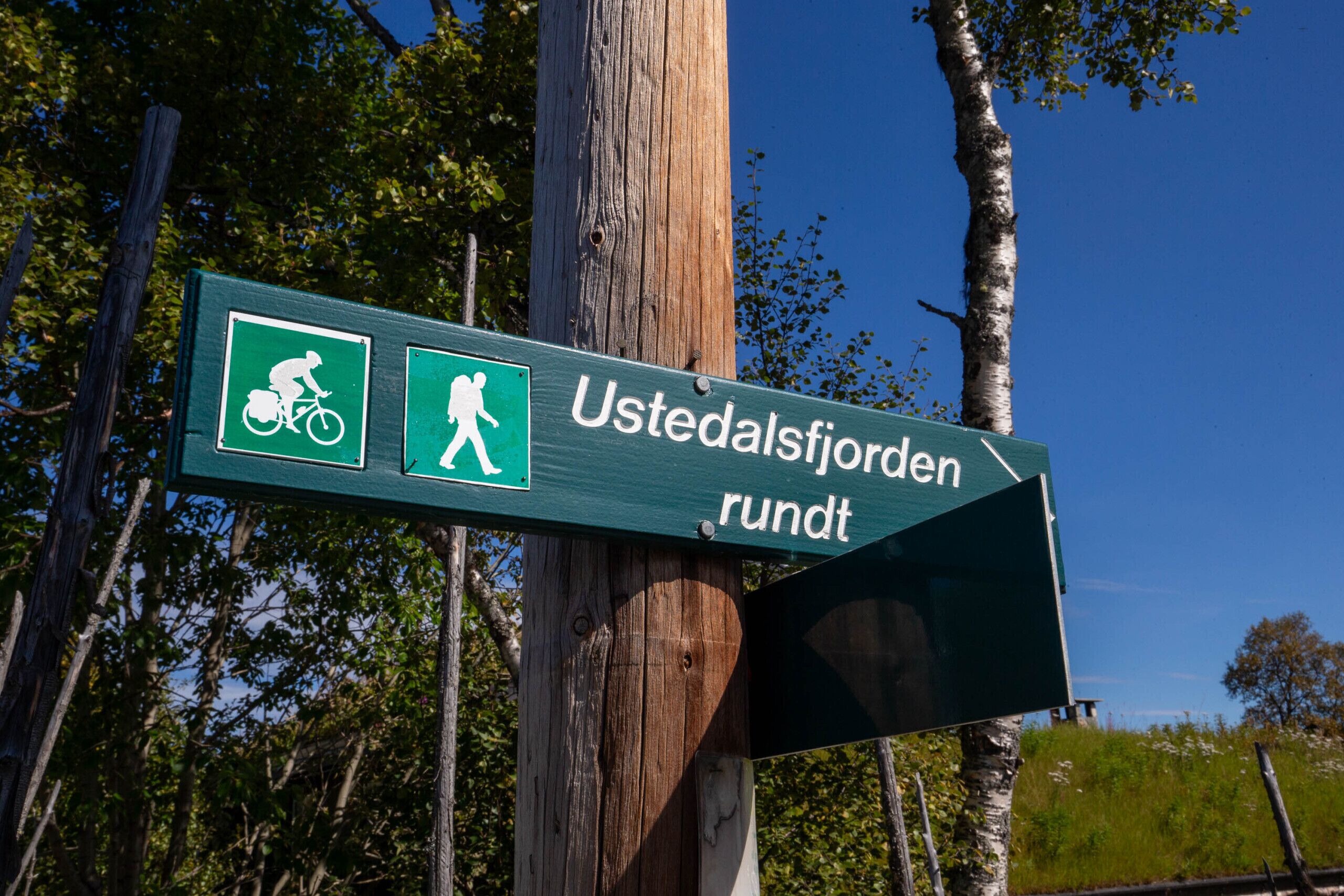A directional sign with symbols for cycling and hiking, indicating a trail or park area.