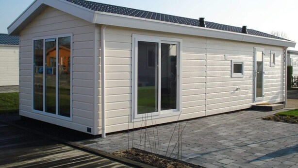 A single-story mobile home with large sliding glass doors, a small attached garage, and a sloped roof. - Holiday Home in Dordrecht With Terrace (Dordrecht)