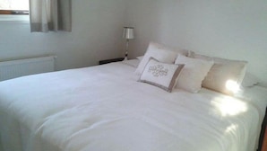 A neatly made bed with white bedding and decorative pillows, a bedside lamp, and a window with curtains. - Holiday Home in Dordrecht With Terrace (Dordrecht)
