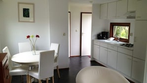 A modern kitchen with white cabinets, a dining area with a round table and chairs, and a view of the outdoors through a window. - Holiday Home in Dordrecht With Terrace (Dordrecht)