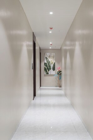 Um corredor com piso branco, um quadro na parede e um vaso com flores.
