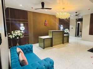 A reception area with a blue sofa, a reception desk, a chandelier, and a wall-mounted sign. - Grand Dularia (Nagpur)