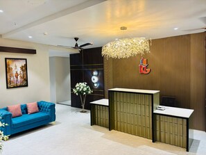 A reception area with a modern design, including a blue sofa, a reception desk, and a decorative light fixture. - Grand Dularia (Nagpur)