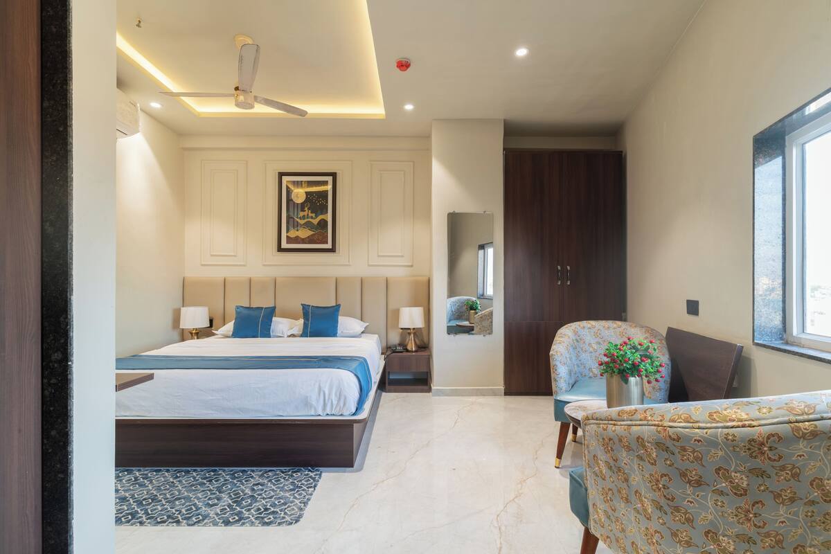 A hotel room with a large bed, a desk, a chair, a mirror, and a window.