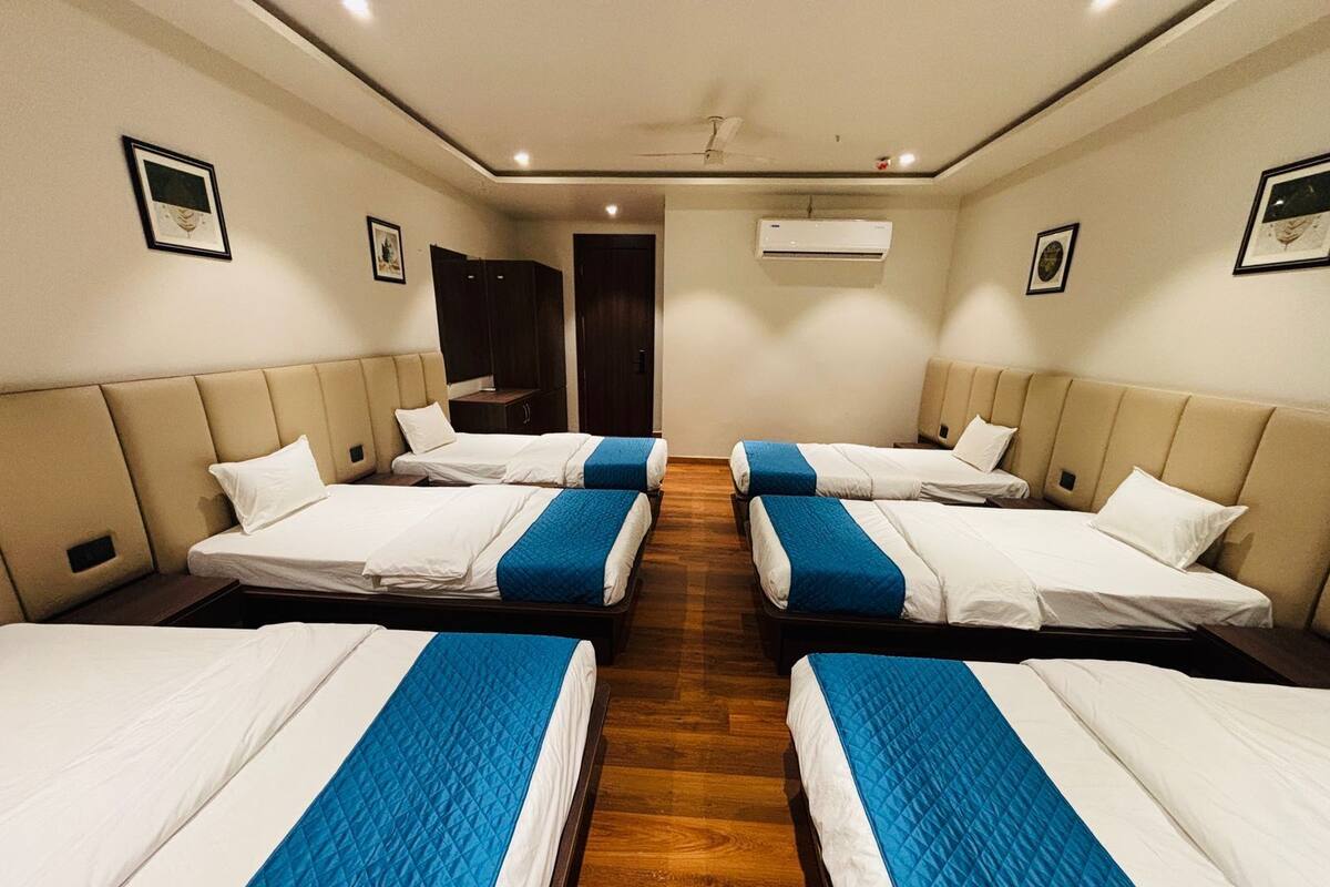 A hotel room with four beds arranged in a row, a wooden floor, and an air conditioning unit on the wall.