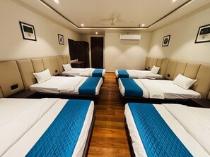 Hotellihuone, jossa on neljä sängyä rivissä, puulattia ja ilmastointilaite seinällä.