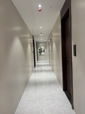 A hallway with white walls, a marble floor, and a door on the right. - Grand Dularia (Nagpur)