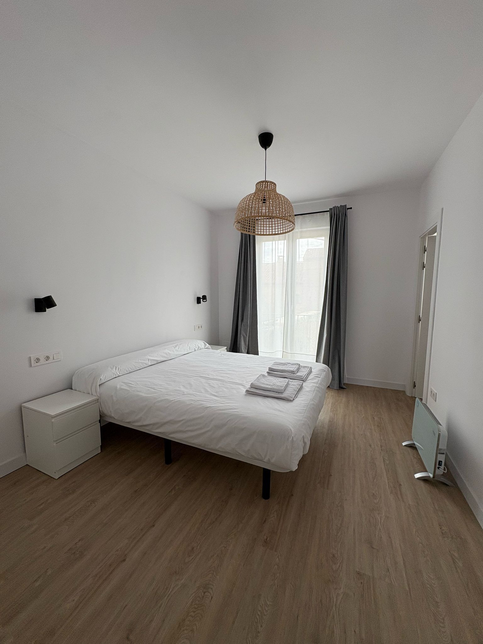 A bedroom with a bed, bedside tables, a wardrobe, a hanging light fixture, and a window with curtains.