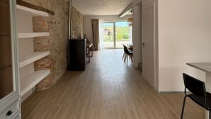 Ein geräumiges Zimmer mit Steinwand, Holzboden, einem Essbereich mit Stühlen und Blick durch ein großes Fenster.