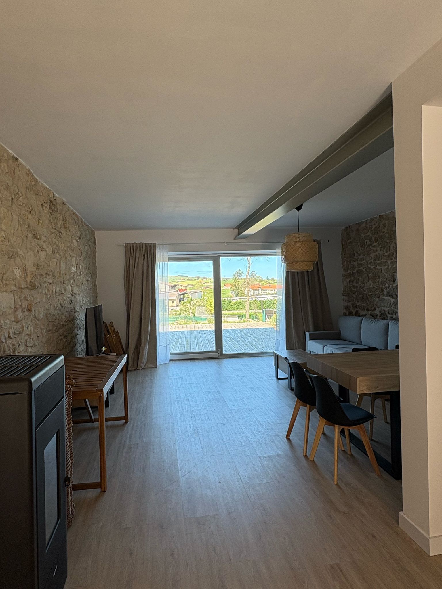 Una habitación amplia con una mesa de madera para comer, sillas, un televisor y una pared de piedra.