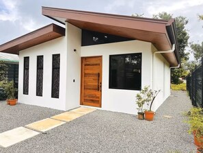 A modern house with a wooden door, large windows, and a gravel driveway. - New cozy private home near all beaches (Uvita)