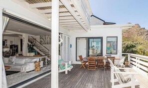 Ett modernt hus med en träveranda, en matplats och en trappa som leder upp till ett övre plan.