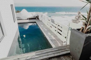 En pool med ett trädäck, en vit byggnad och utsikt över havet.