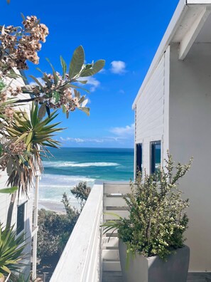 Een balkon met uitzicht op de oceaan, een wit gebouw en een plantenbak met groene planten.