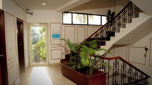 Un pasillo con escalera de madera, mostrador de recepción y un cartel con los números y la ubicación de las habitaciones.