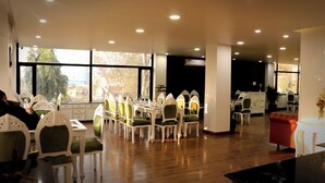 Un comedor con mesas y sillas, un sofá y un ventanal con vista a árboles.