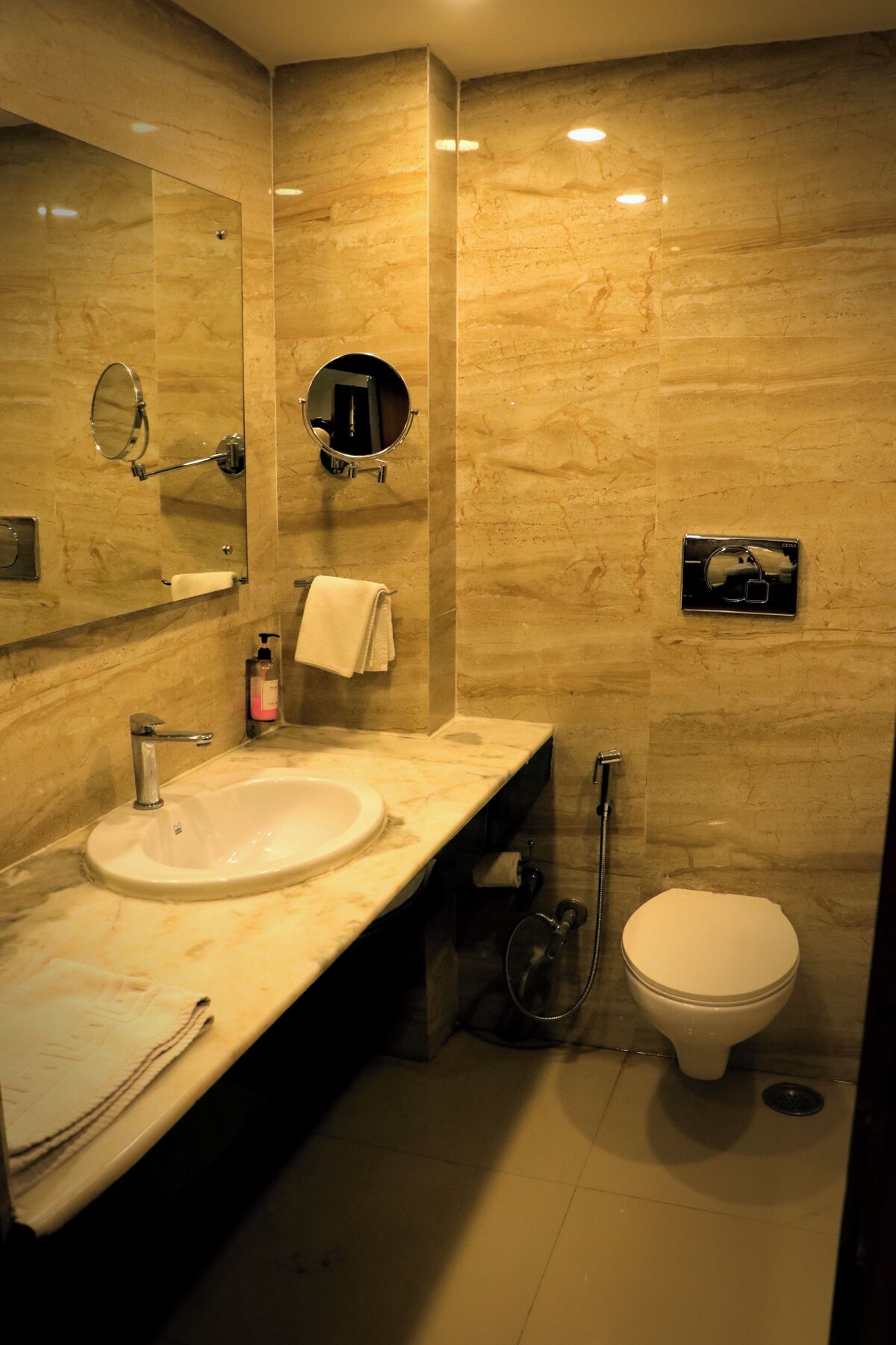 Une salle de bain moderne avec un lavabo en marbre, des toilettes, une douche et deux miroirs.